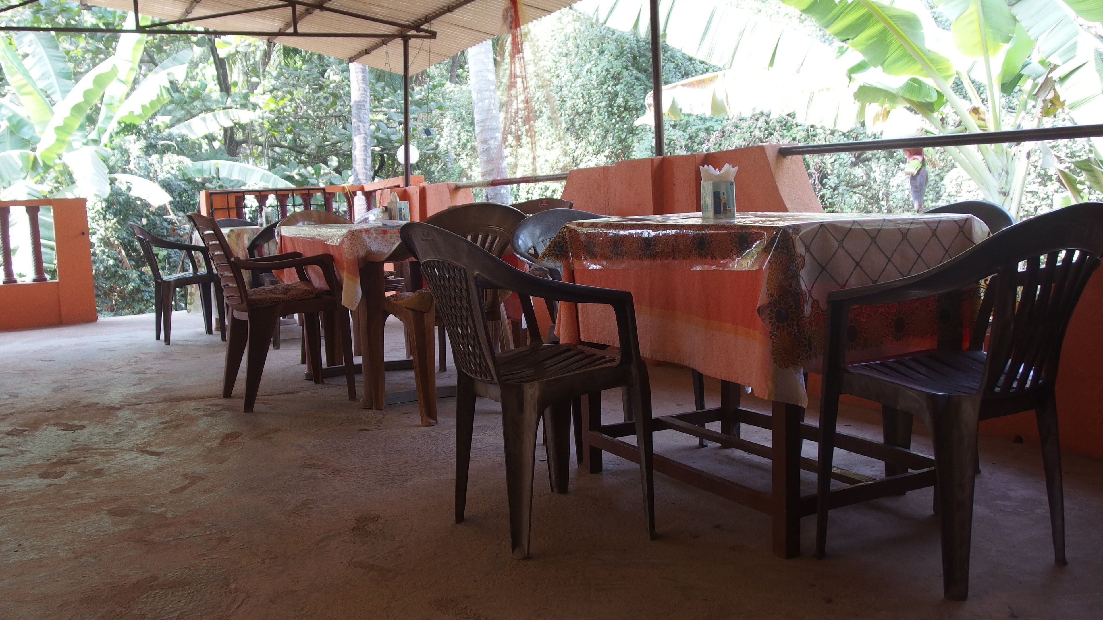 An outdoor dining area with tables and chairs, surrounded by lush greenery.