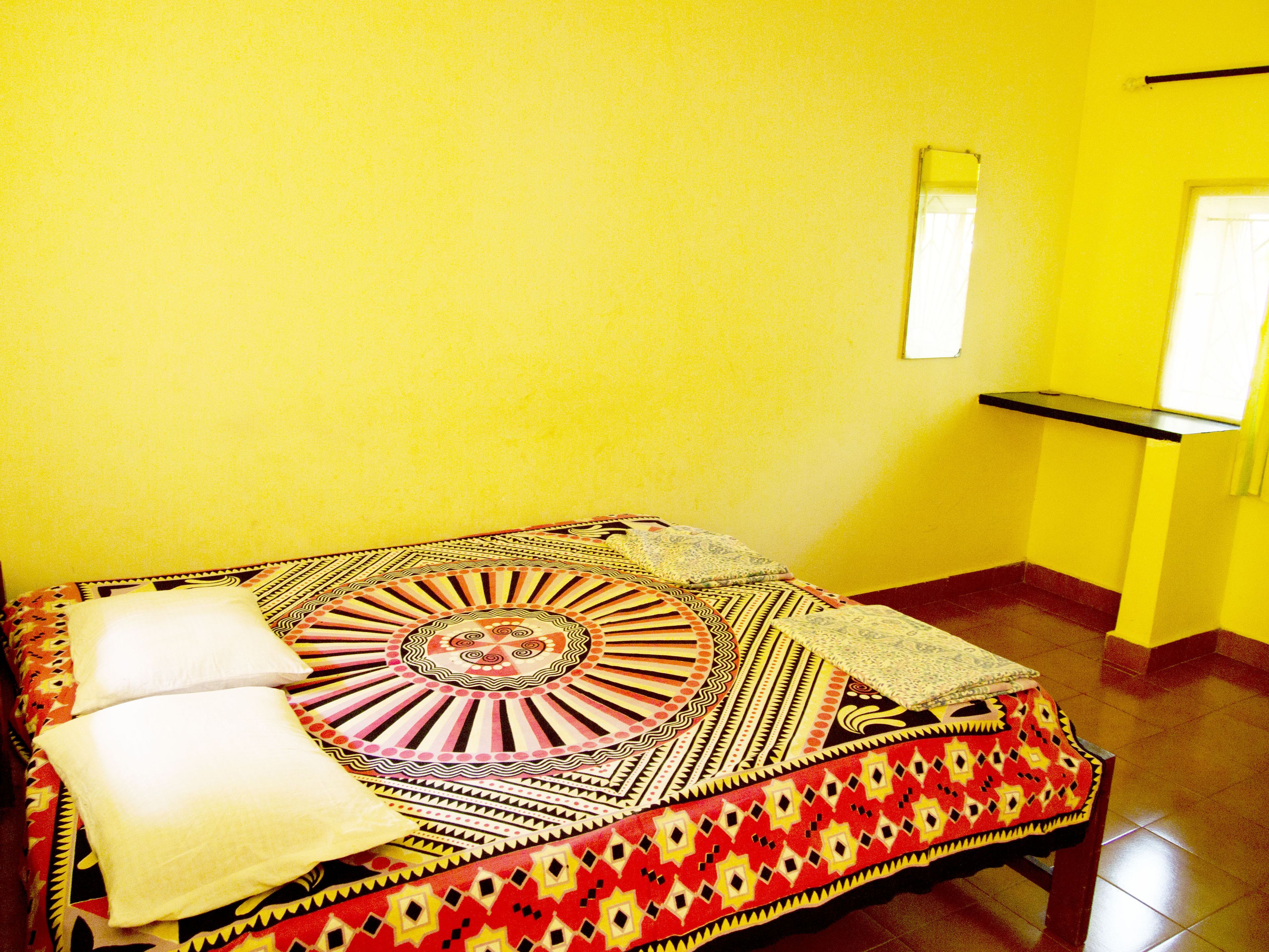 A room with a bed covered in patterned blankets and pillows, a small table with a tray, and a window with curtains.