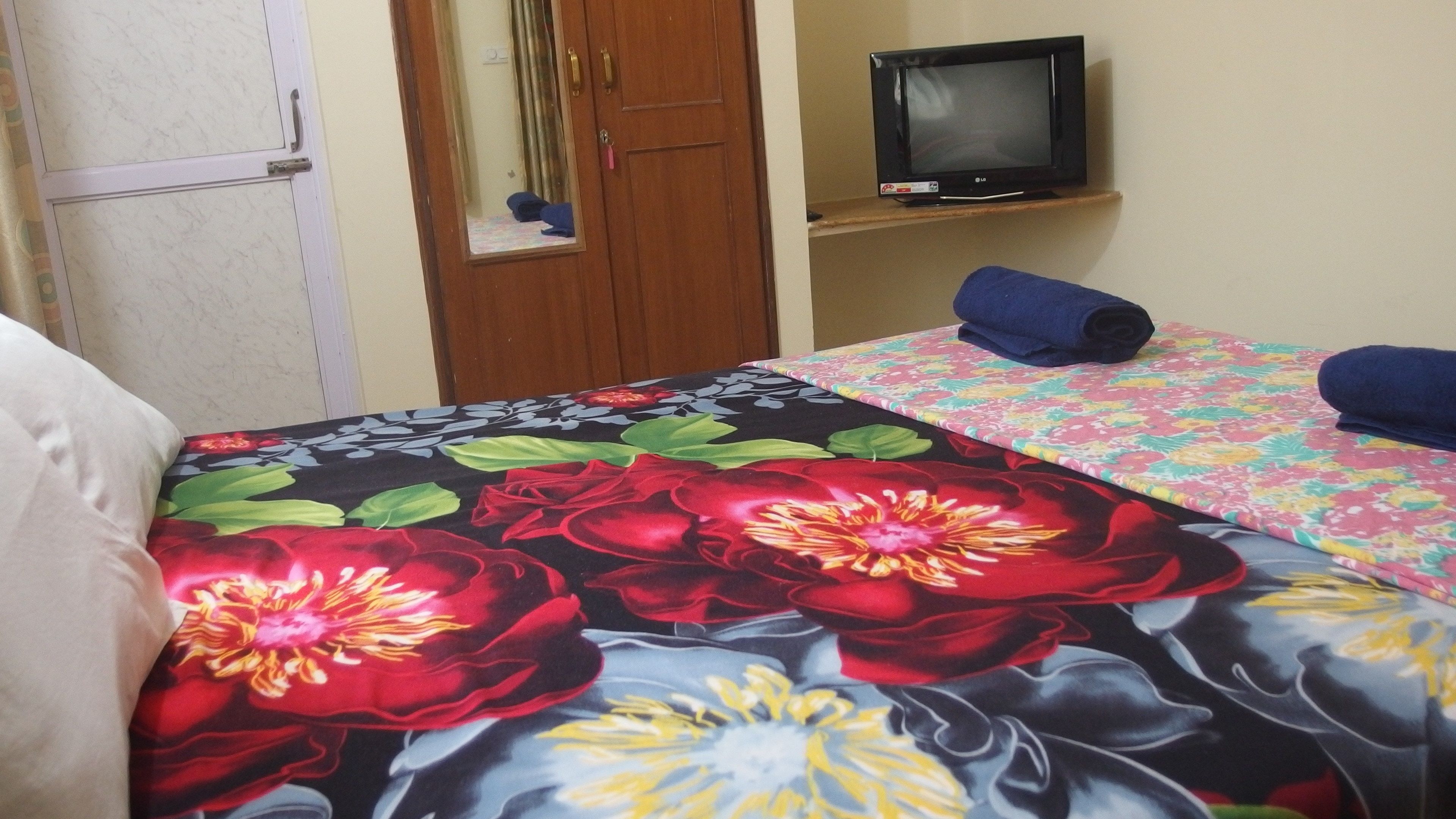 Una habitación de hotel con una cama, un televisor sobre un mueble bajo y una puerta con espejo.