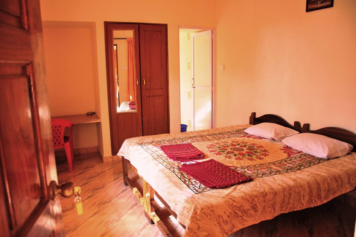 Une chambre à coucher avec un lit, une porte en bois, une chaise rouge et une armoire.