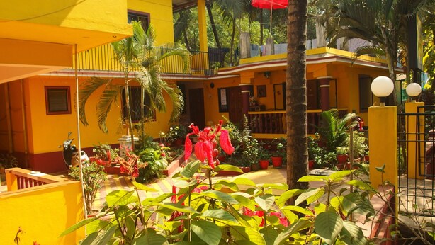 A courtyard with yellow buildings, potted plants, and a red umbrella. - Yellow House (Vagator)