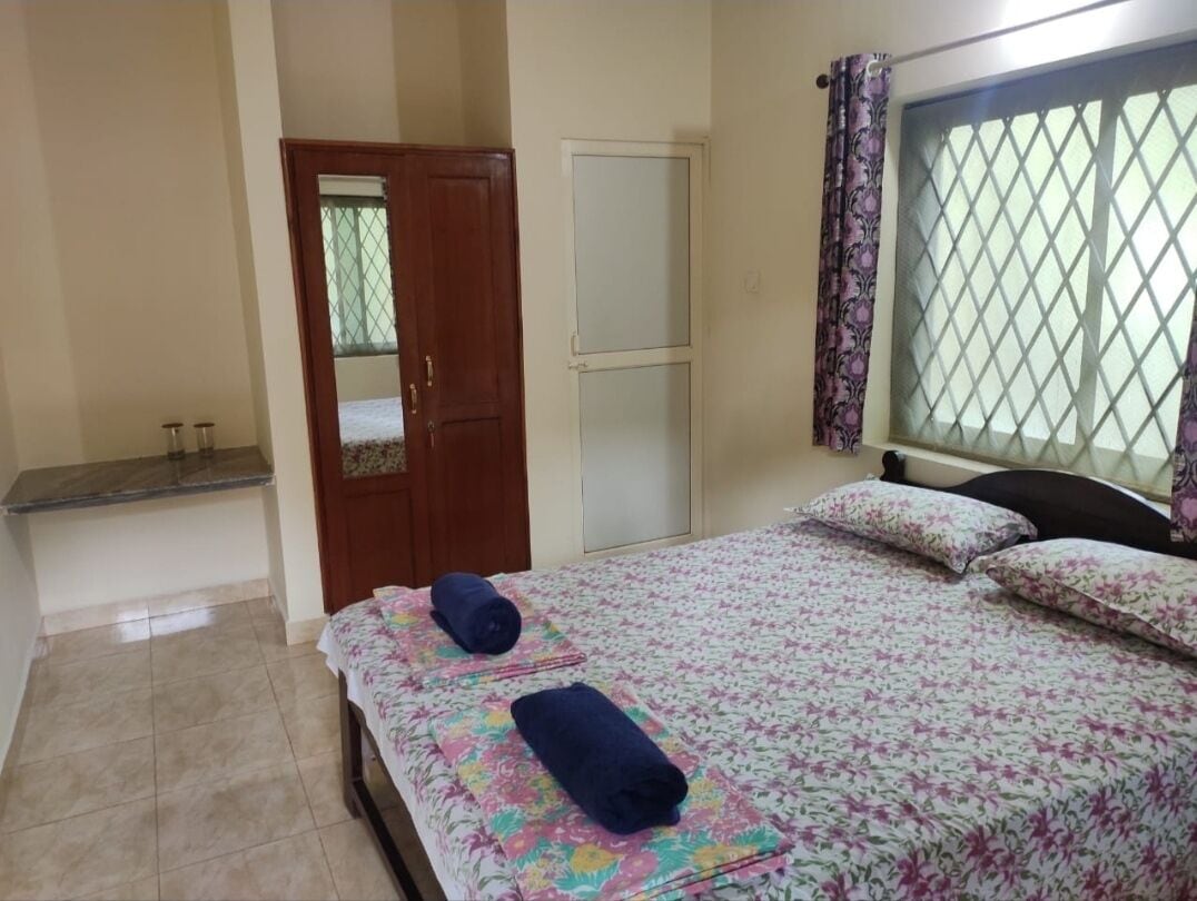 A bedroom with a bed, a wardrobe, a mirror, and a window with a curtain.