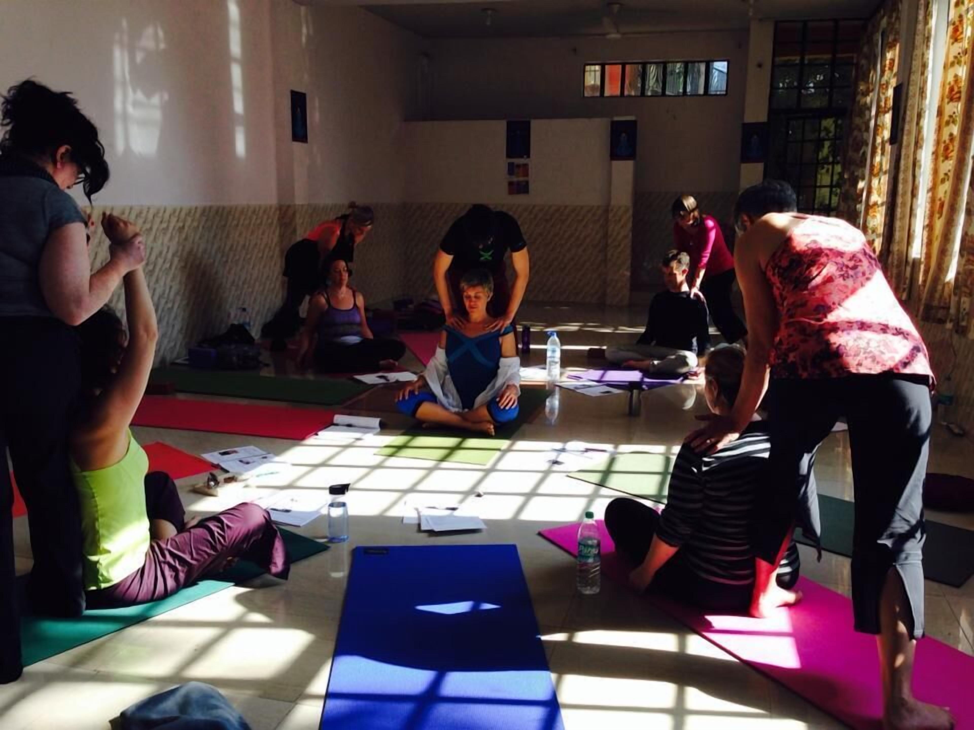 Un cours de yoga dans une salle dotée de grandes fenêtres, de tapis et où se trouvent les participants.