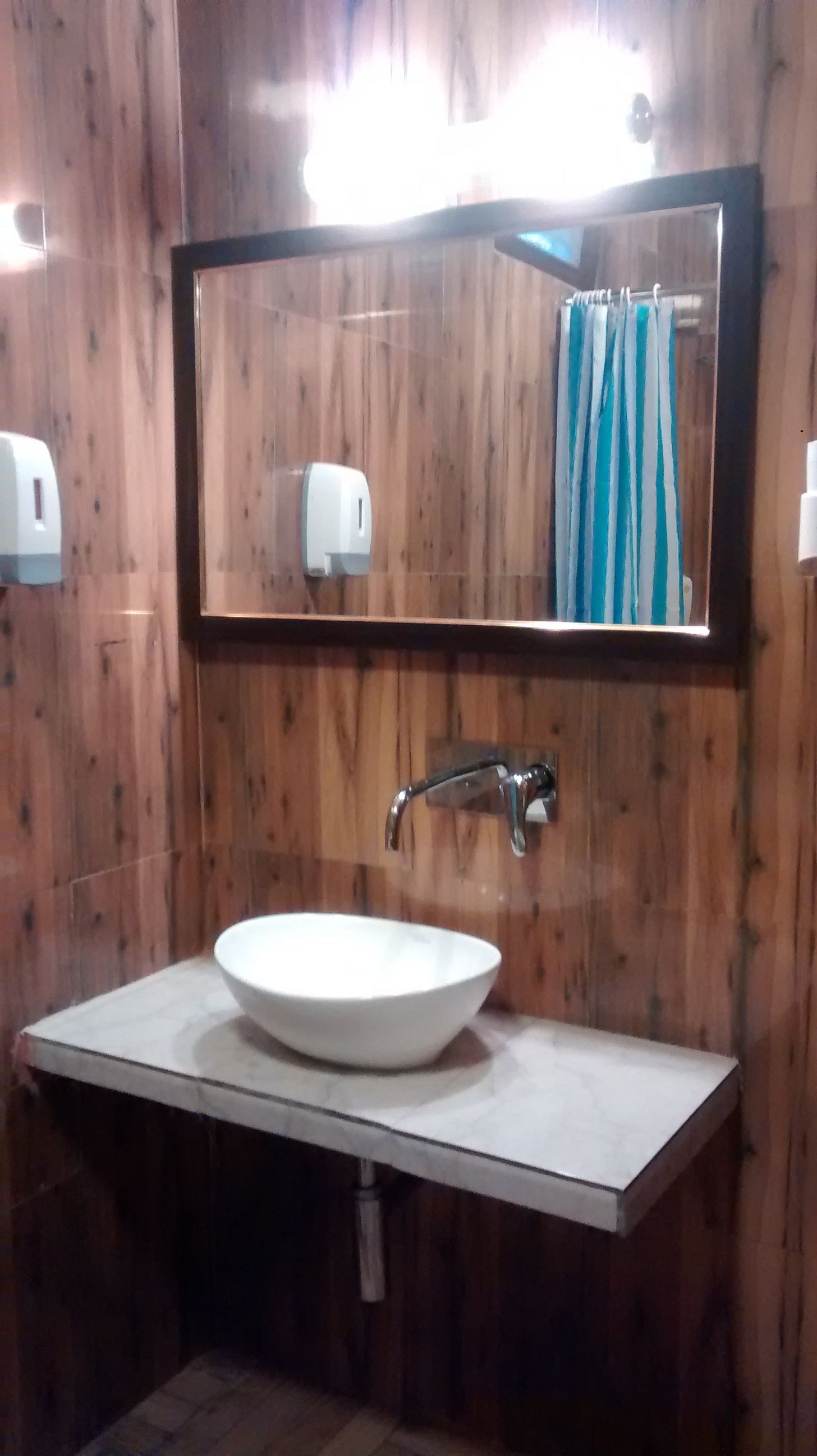A bathroom with a wooden wall, a white sink, a mirror, and a towel rack.