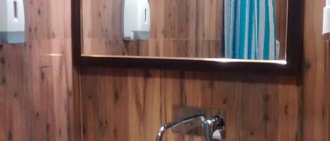 A bathroom with a wooden wall, a white sink, a mirror, and a towel rack.