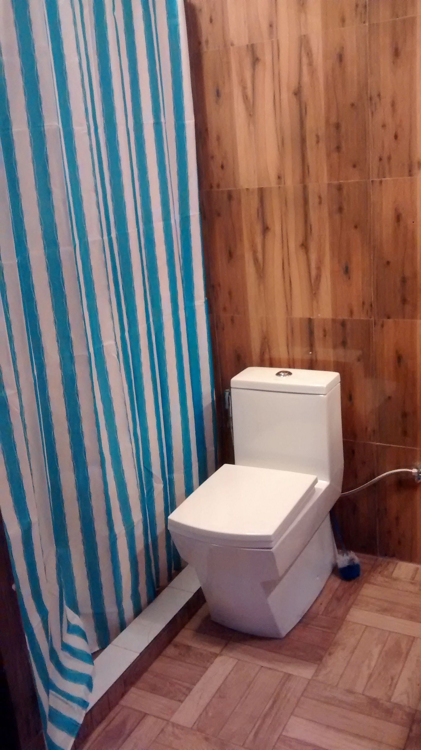 A bathroom with a white toilet, a striped shower curtain, and wooden paneling on the wall.