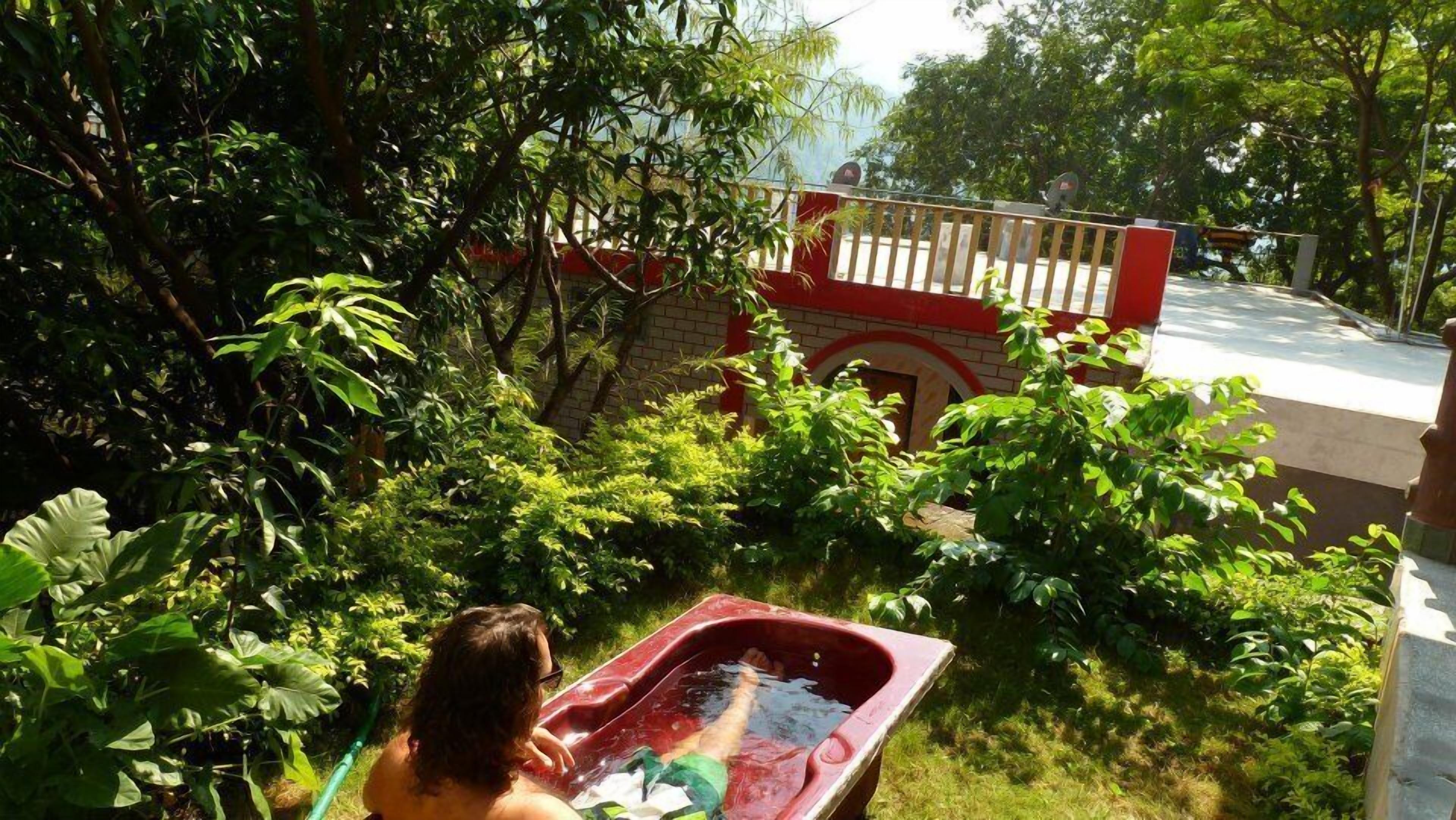A garden with a red tub, dense foliage, and a red and white building with a balcony.