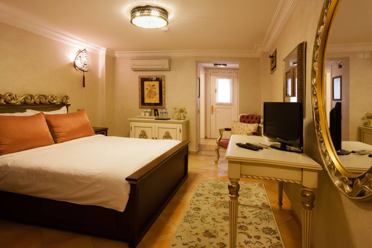 Quarto de hotel com uma cama grande, uma escrivaninha com computador, televisão e um espelho.