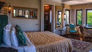 Een slaapkamer met een bed, een televisie, een bureau en een uitzicht op de stad door grote ramen.