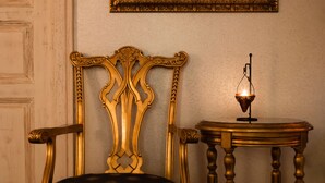 Een kamer met een vintage stoel, een klein tafeltje met een kaars, en een kunstwerk in een lijst aan de muur.