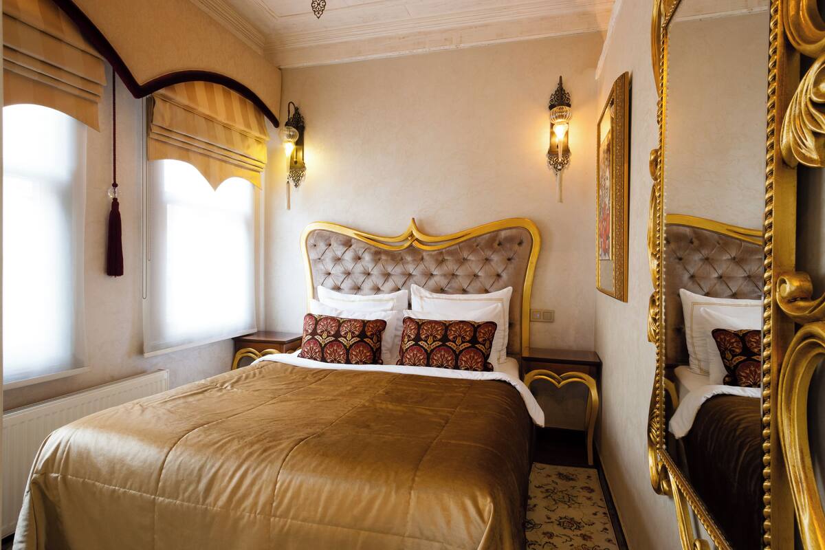 Um quarto luxuoso com uma cama grande, cabeceira decorada e arandelas na parede.