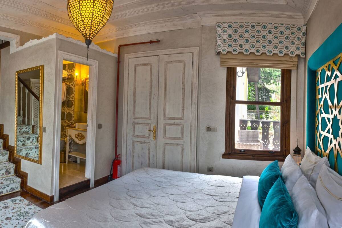 Quarto com cama, escada, espelho, janela e porta.