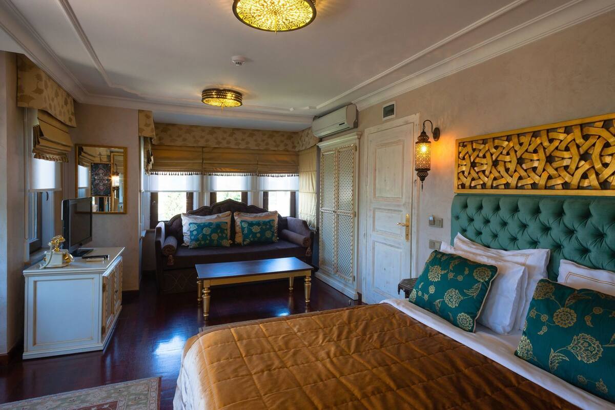 Quarto de hotel com cama, sofá, escrivaninha e televisão.
