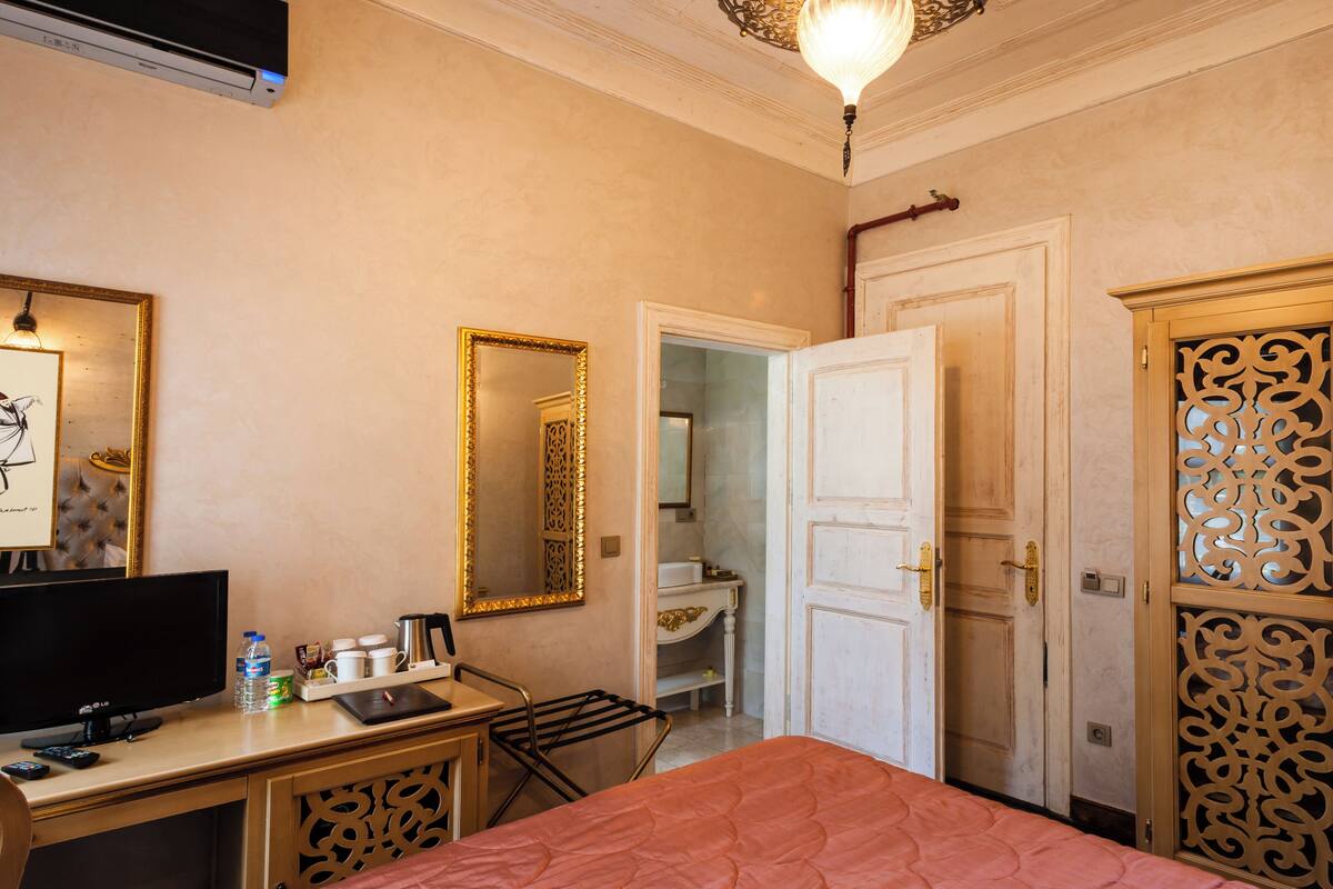 Quarto de hotel com cama, escrivaninha com televisão, espelho e guarda-roupa.