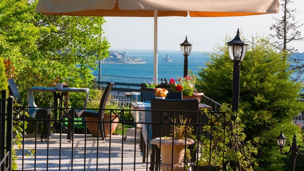 Een terras met zitplaatsen buiten, plantenpotten en uitzicht op zee.