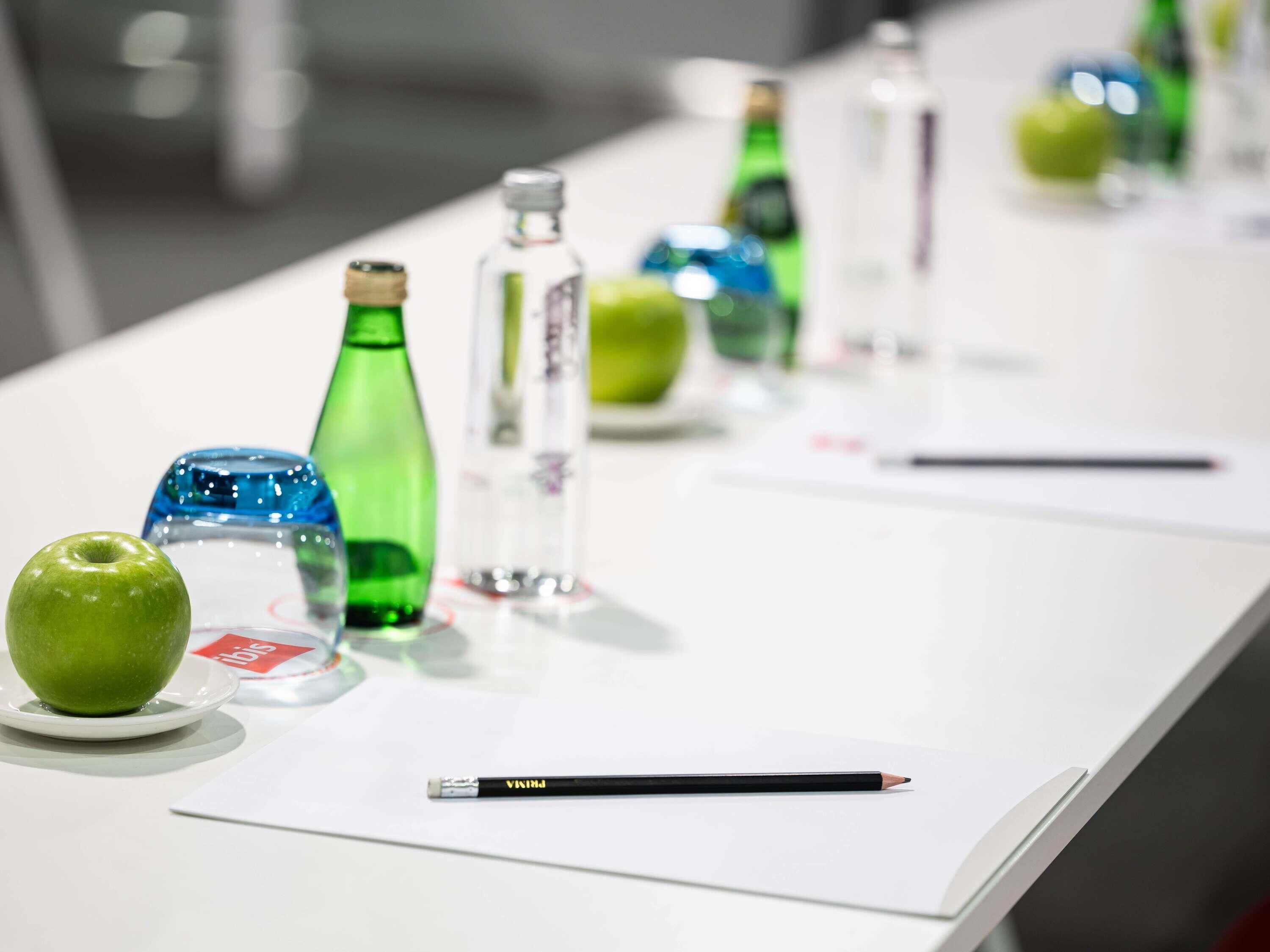 Uma mesa com vários objetos, incluindo uma maçã verde, um copo azul e um lápis preto.