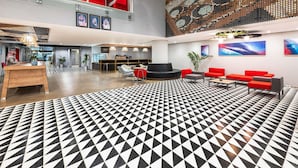 Un vestíbulo moderno con suelo de diseño geométrico, asientos rojos, un mostrador de recepción y una gran obra de arte en la pared.