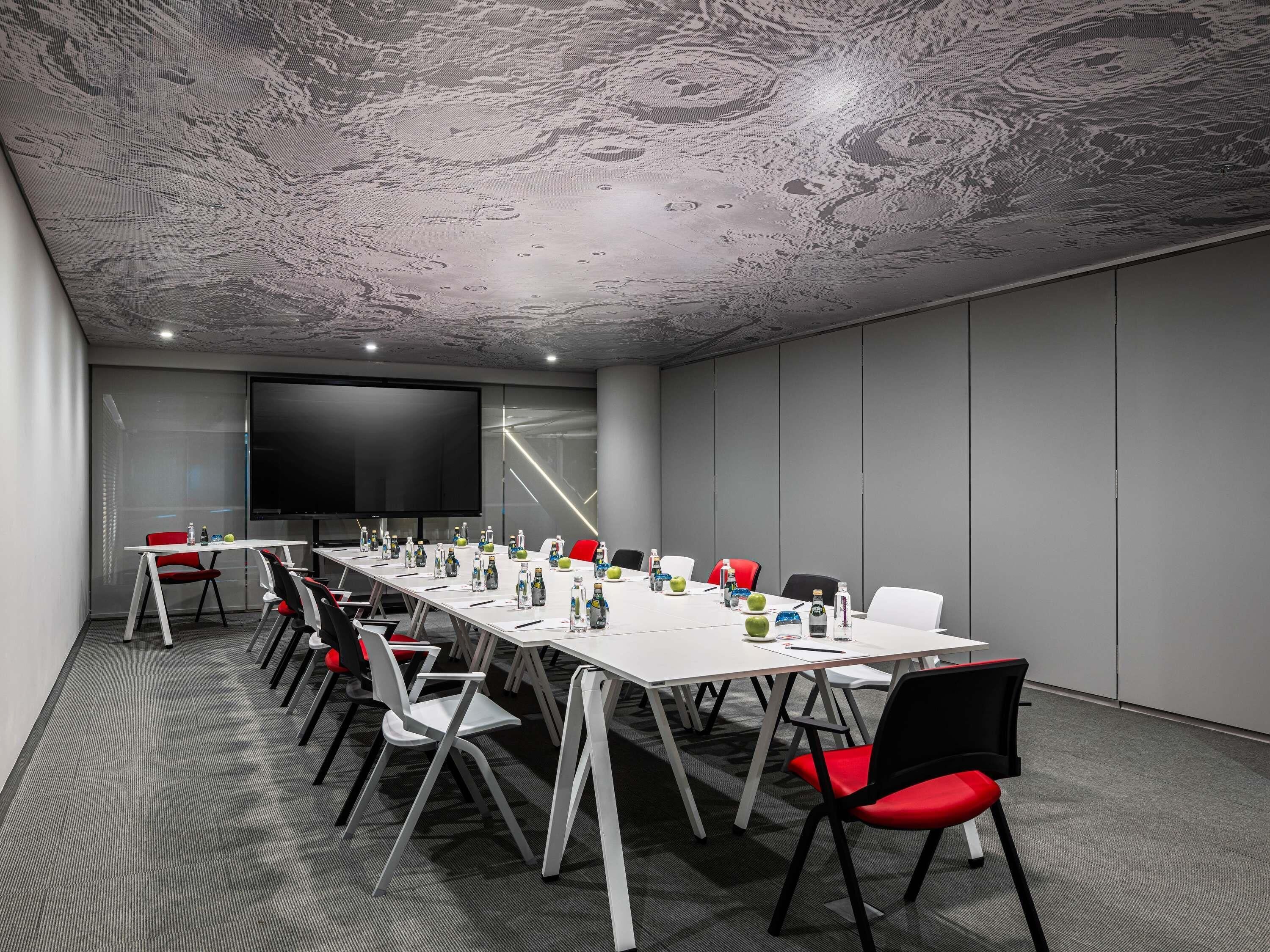 A conference room with a long table, multiple chairs, a large screen, and a textured ceiling.