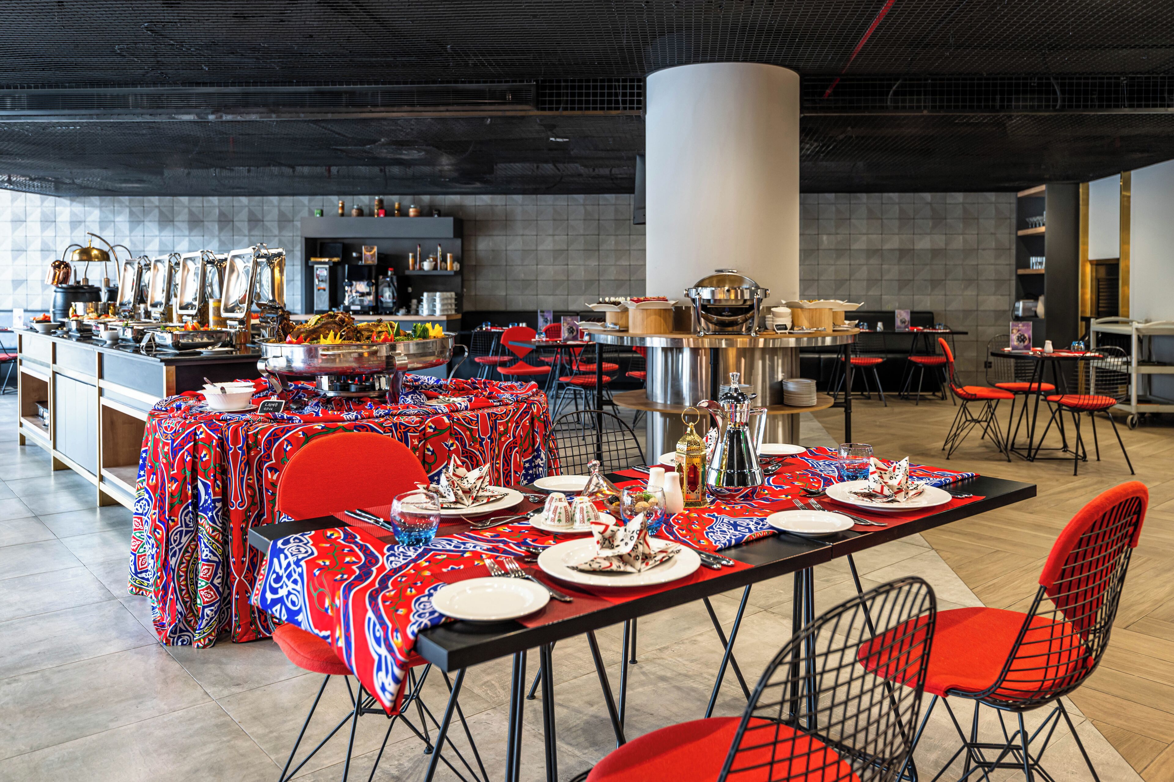 A dining area with tables set for meals, red chairs, and a kitchen in the background.