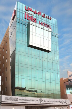 Un hôtel moderne avec une façade en verre et une enseigne bien visible indiquant qu’il s’agit d’un hôtel ibis.