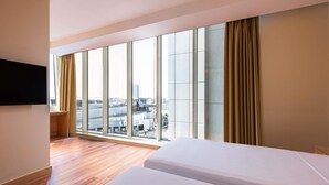 A hotel room with a large window, a flat-screen TV, and a wooden floor. - Ibis Riyadh Hotel Al Muhammadiyah United Company Branch (Riyadh)