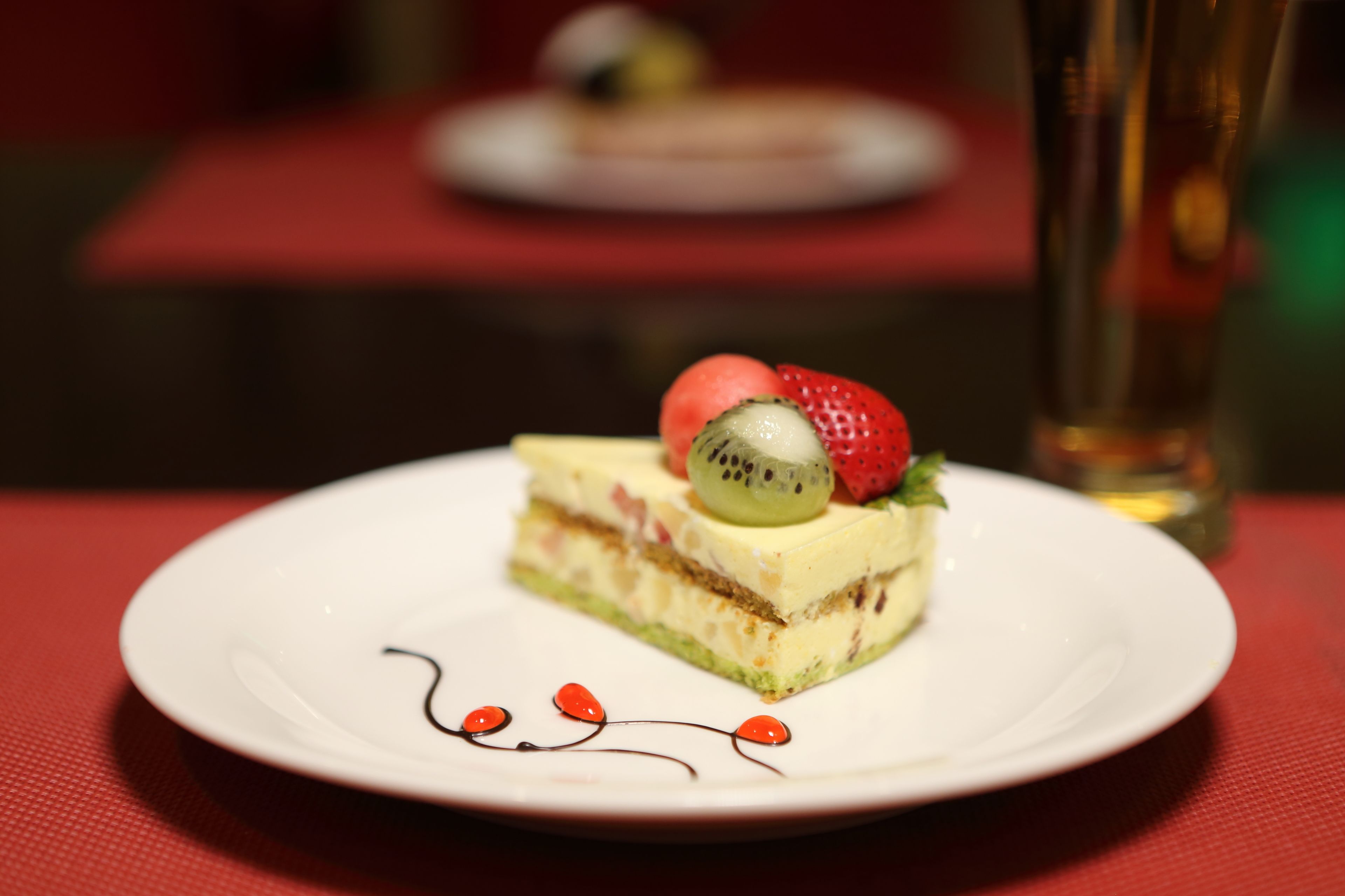 Una porción de pastel en un plato blanco con frutas, sobre un mantel rojo.