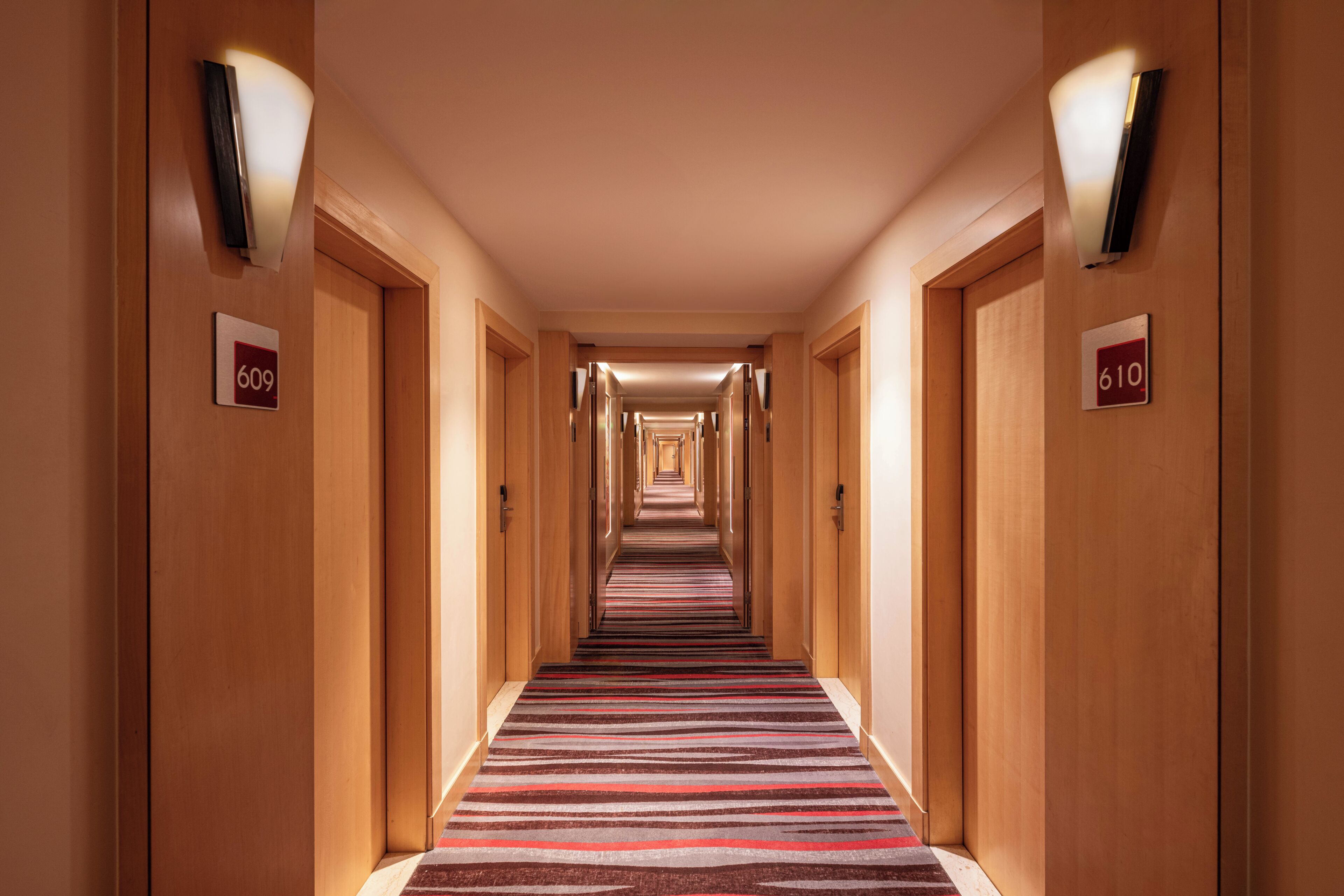 Un pasillo de hotel con paredes de madera, puertas numeradas y alfombra a rayas.