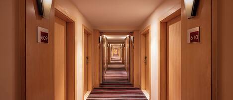 Un pasillo de hotel con paredes de madera, puertas numeradas y alfombra a rayas.