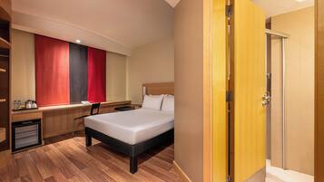 Quarto de hotel com cama, escrivaninha, cadeira e guarda-roupa.