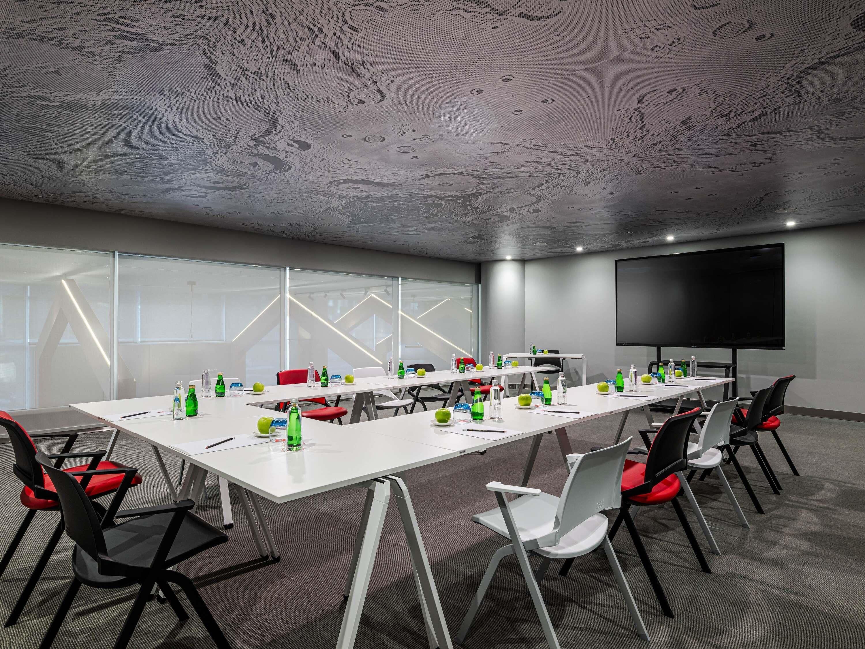 A conference room with a long table, chairs, a projector screen, and glass walls.