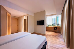 Habitación de hotel con cama, televisor, escritorio y vista a edificios altos.