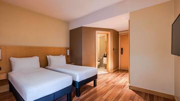 Habitación de hotel con dos camas, cabecero de madera, mesita de noche, televisor de pantalla plana y piso de madera.