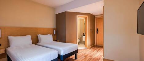 A hotel room with two beds, a wooden headboard, a nightstand, a flat-screen TV, and a wooden floor.