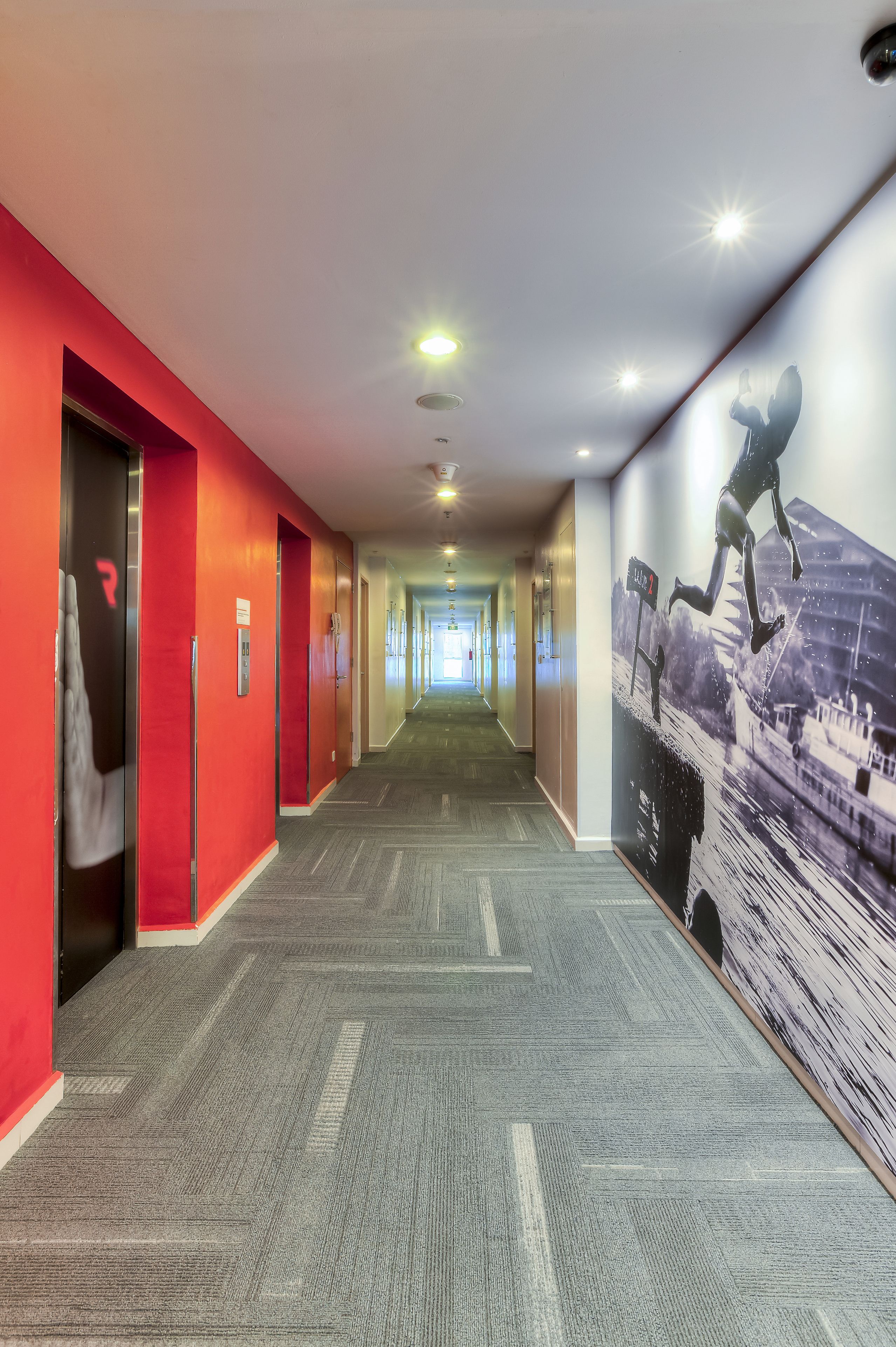 A long hallway with red walls, a carpeted floor, and a large mural of a runner on the right wall.