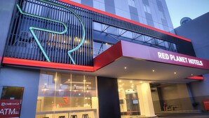 Un hôtel à la façade moderne, avec une enseigne bien visible indiquant « Red Planet Hotels », et un distributeur automatique de billets situé sur le côté gauche.