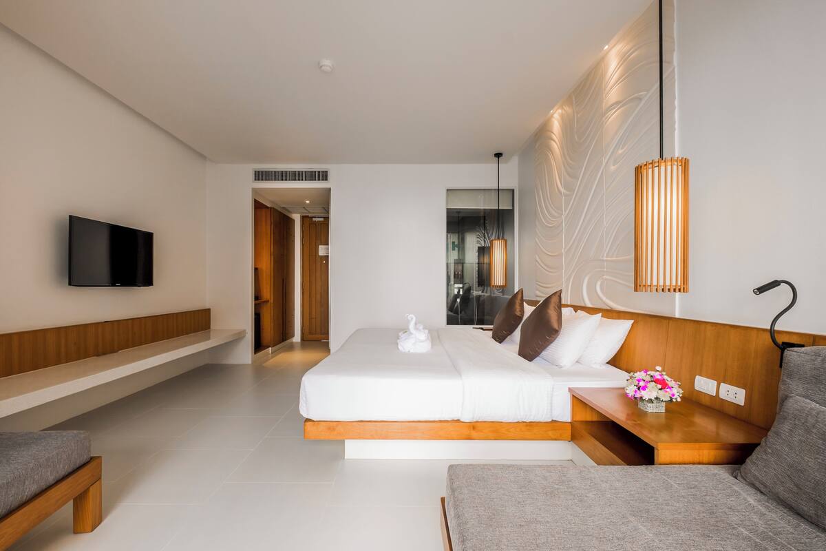 Une chambre d’hôtel moderne dotée d’un grand lit, d’un téléviseur à écran plat fixé au mur, d’un banc en bois et d’un canapé.