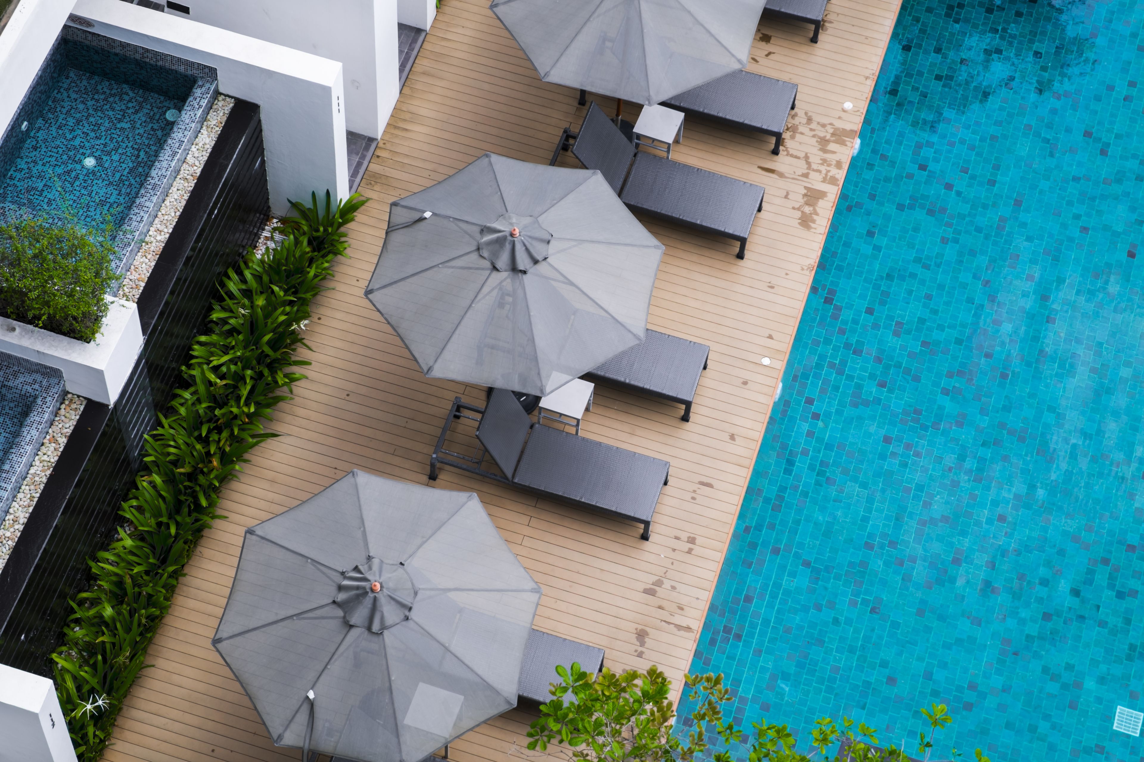An aerial view of a poolside area with multiple lounge chairs and umbrellas, surrounded by a wooden deck and a swimming pool.