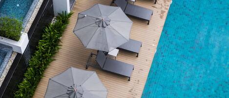 An aerial view of a poolside area with multiple lounge chairs and umbrellas, surrounded by a wooden deck and a swimming pool.
