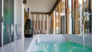 Een moderne badkamer met een groot bad, een fles champagne en twee champagneglazen op een aanrecht.
