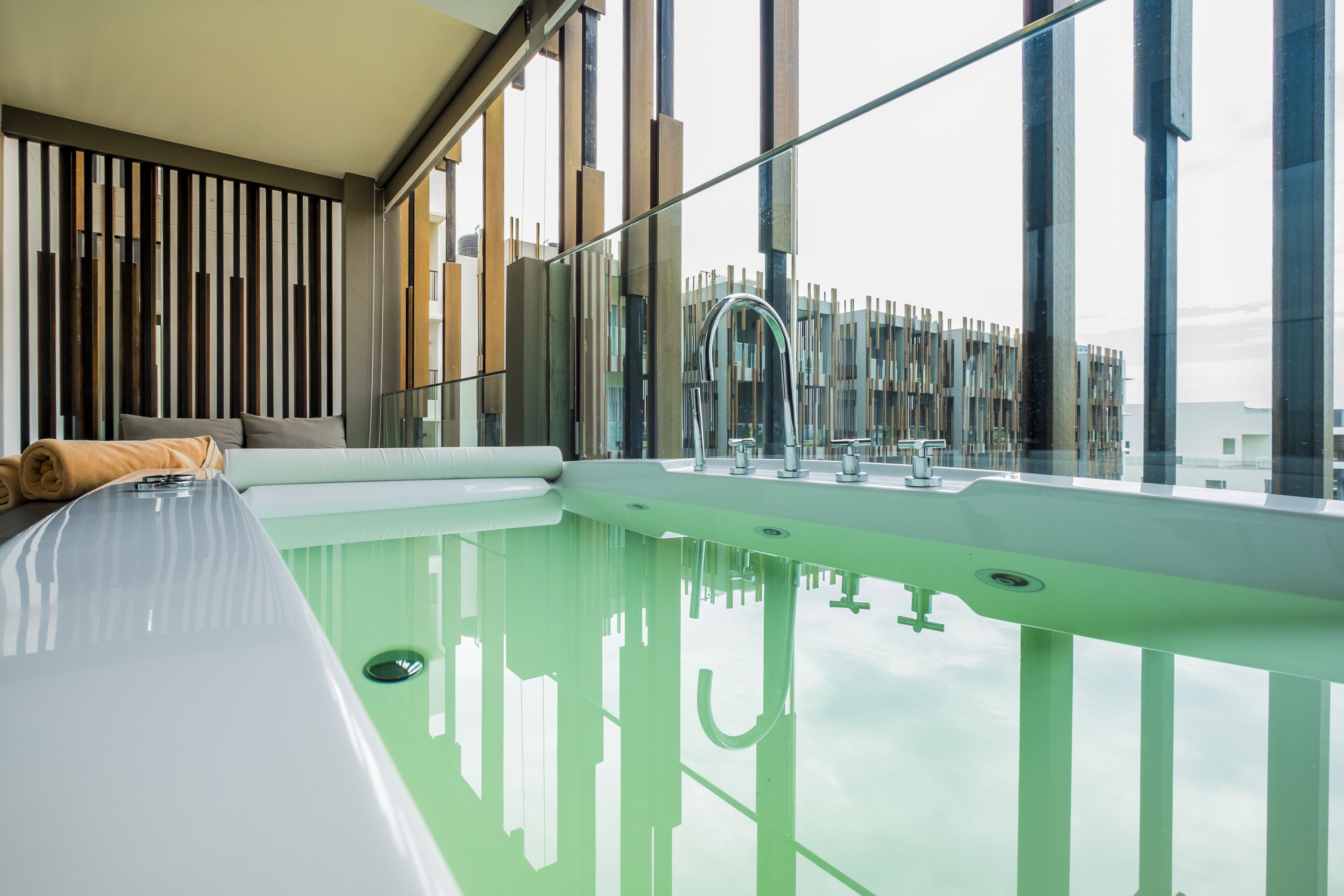 A modern bathroom with a large glass-enclosed bathtub, a wooden slat wall, and a view of a building outside.
