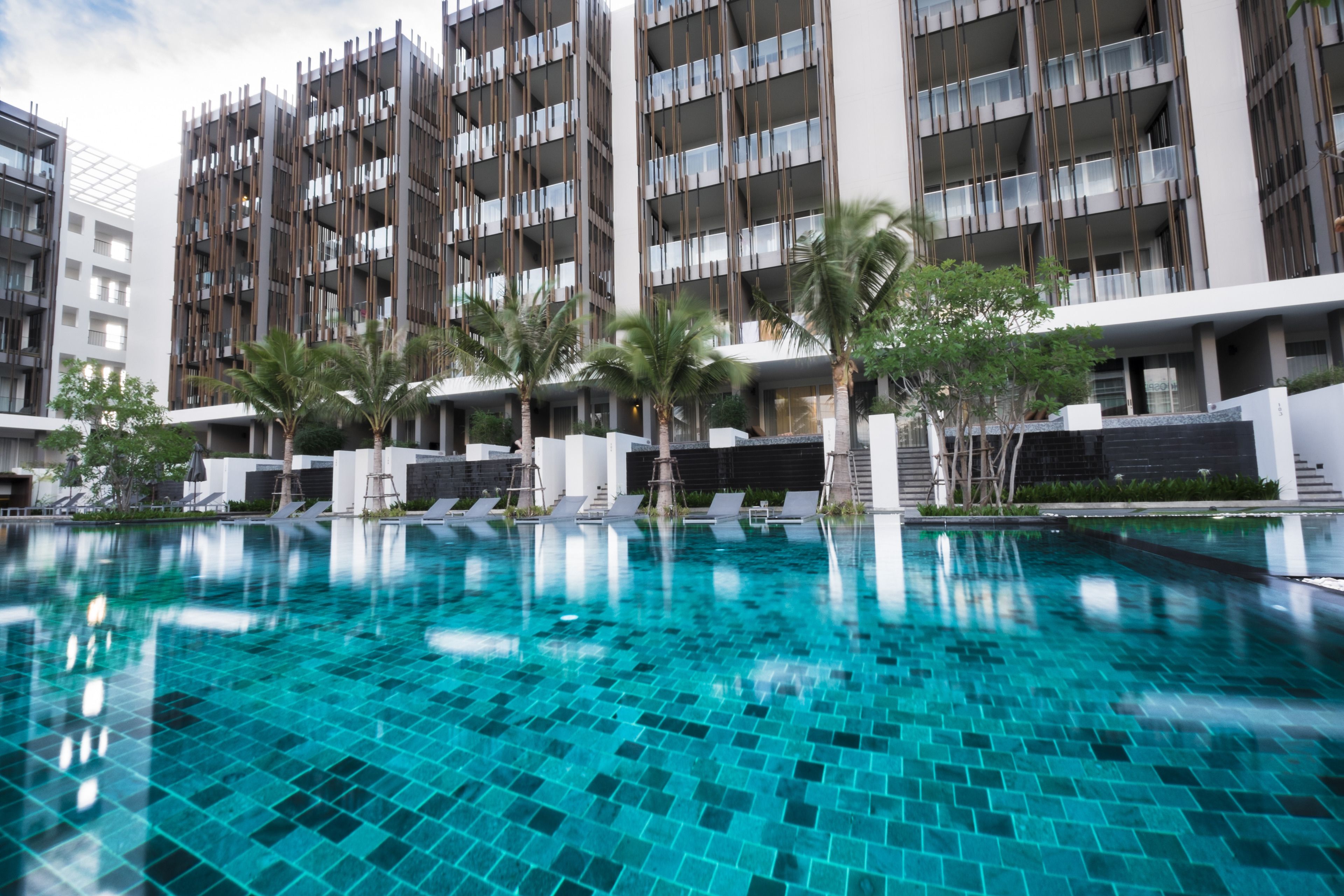 Un hotel moderno con piscina, varios balcones y palmeras.
