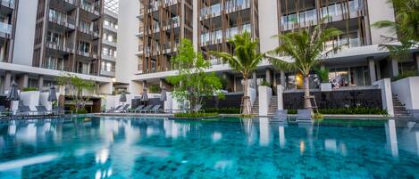 A modern hotel with a swimming pool, multiple balconies, and outdoor seating areas.