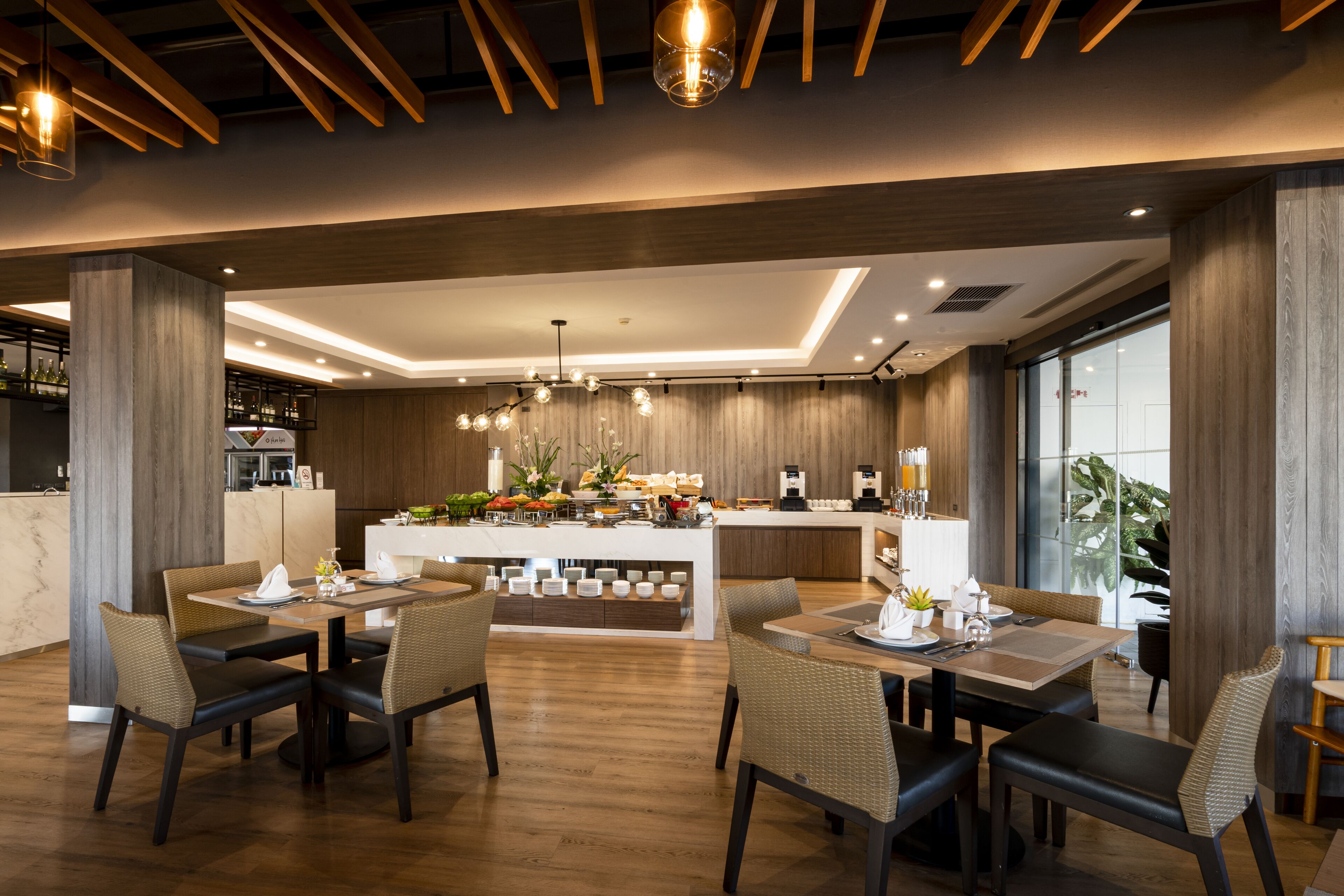 A modern dining area with wooden flooring, dark-toned chairs, and a central island with a bar setup.
