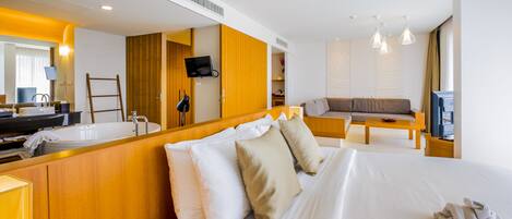 A hotel room with a large bed, a bathroom, a seating area, and a TV.