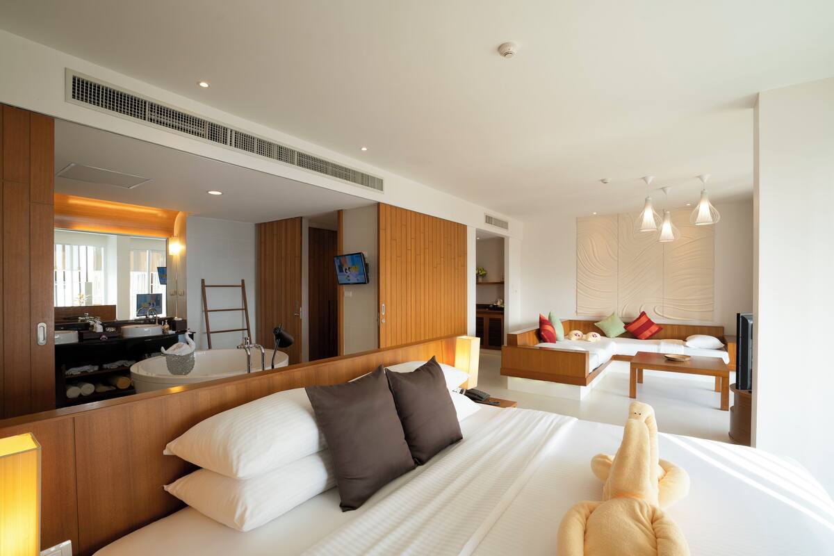 Une chambre d’hôtel moderne dotée d’un grand lit, d’un coin salon avec un canapé et une table basse, d’une télévision et d’une salle de bain avec une baignoire et un miroir.