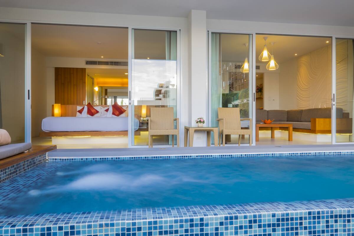Une chambre d’hôtel moderne dotée d’une grande porte-fenêtre coulissante donnant sur un espace de vie, un balcon privé et une piscine.