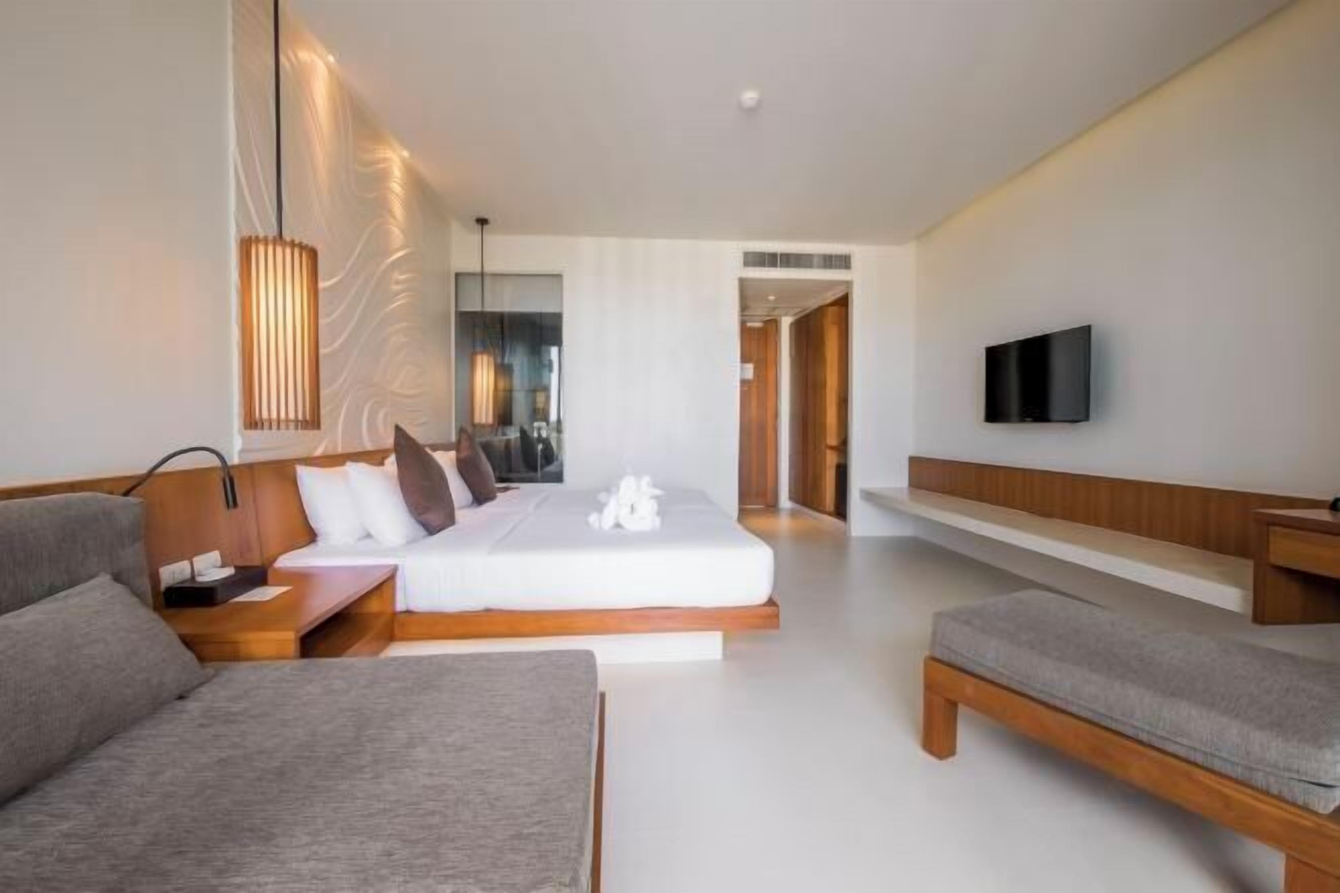 A modern hotel room with a bed, a sofa, a TV, and a bedside table.