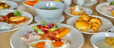 Un bufé de desayuno con diversas opciones, incluyendo huevos, tocino, cruasanes y ensaladas.