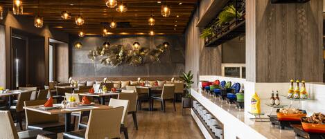 A modern restaurant with wooden ceiling and hanging lights, a buffet with various food items, and a stone wall with decorative elements.