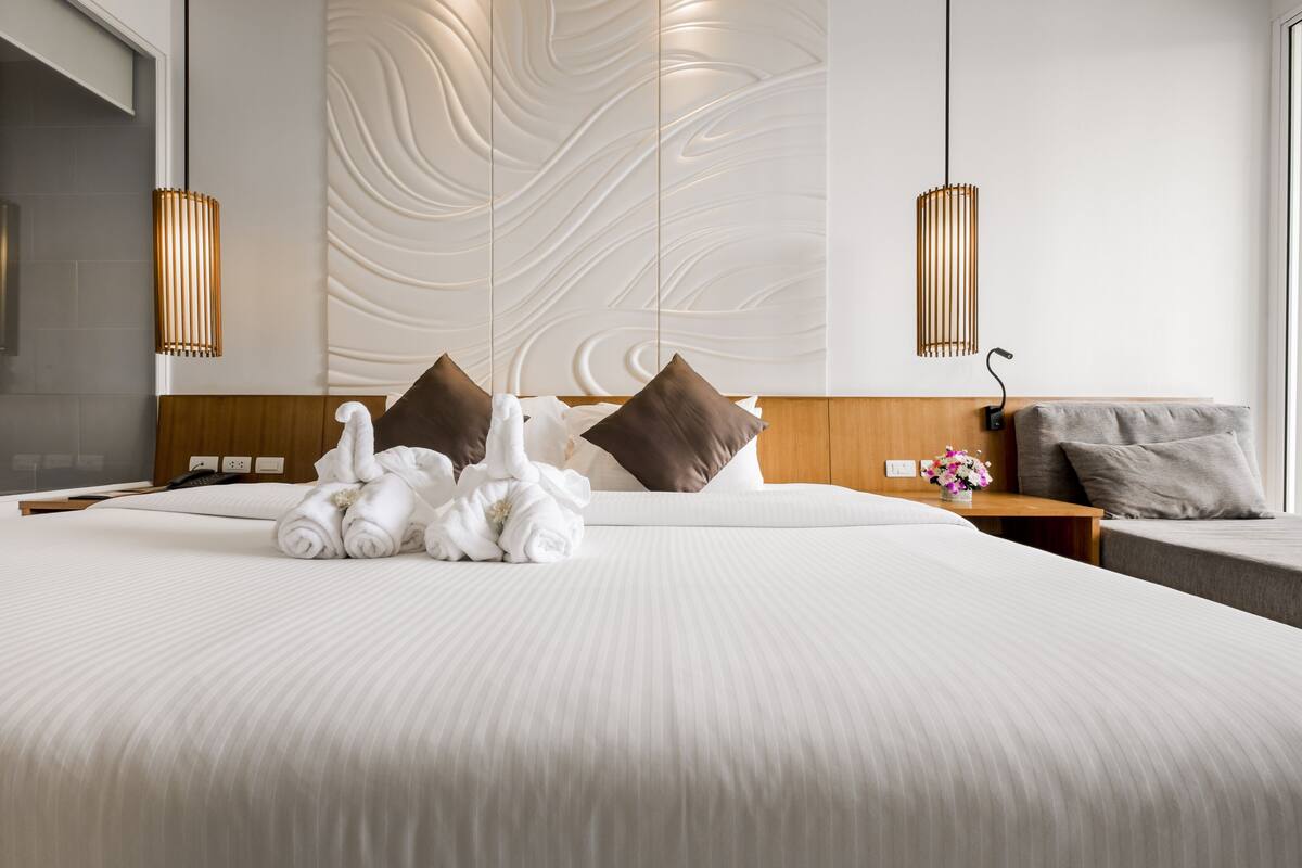 Une chambre d’hôtel avec un grand lit, deux tables de chevet, une tête de lit en bois, un mur au motif texturé et deux lampes suspendues.